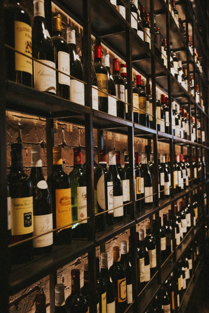 Garrafas de vinho deitadas em prateleira de adega, iluminadas por luz baixa