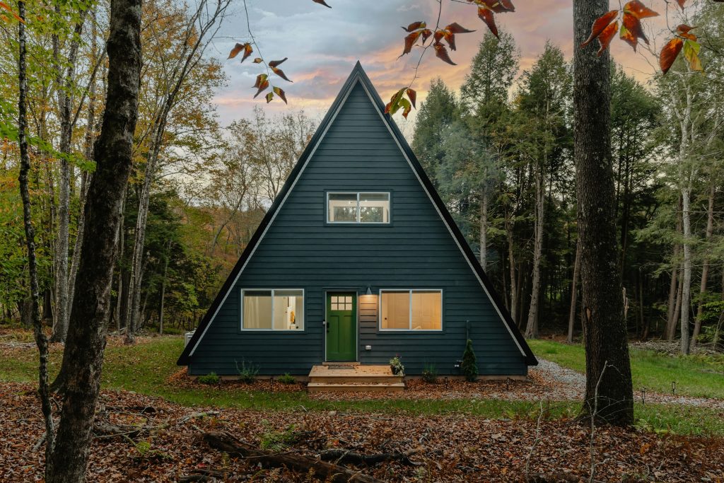 Bangalô de telhado triangular com porta verde entre as árvores, na luz baixa do fim de tarde