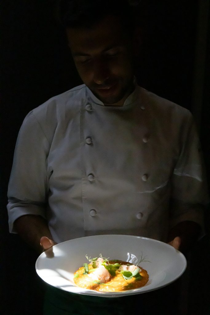 Mãos de chef apresentando um prato recém-finalizado sobre a passagem da cozinha