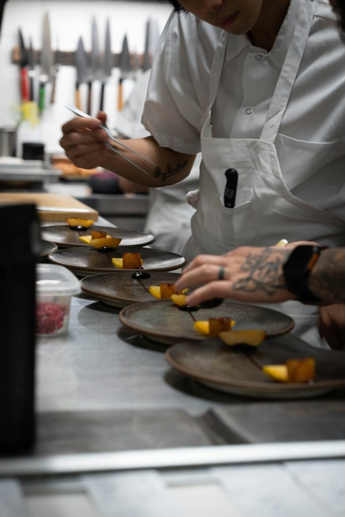 Chef finalizando o empratamento de um prato na bancada de uma cozinha profissional