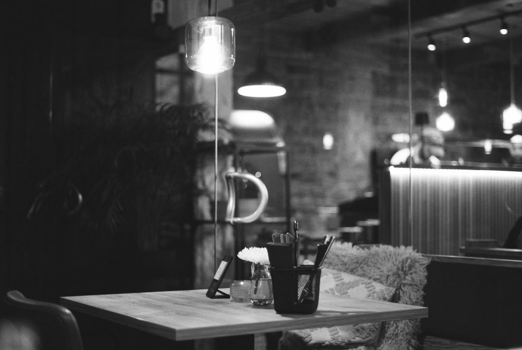 Mesa intimista de restaurante em penumbra, com talheres e copos prontos para o jantar