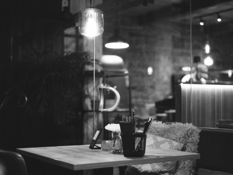 Mesa intimista de restaurante em penumbra, com talheres e copos prontos para o jantar