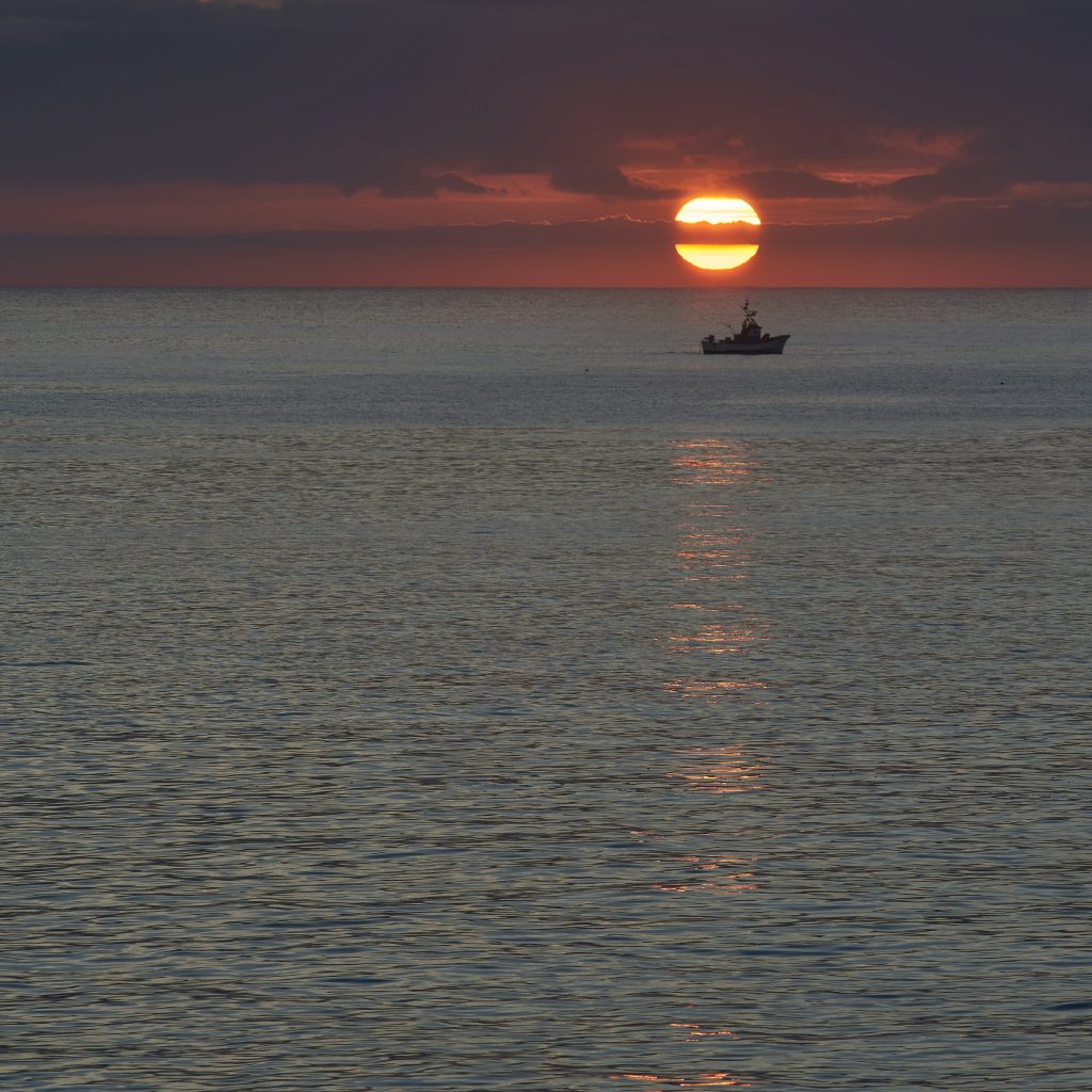 Veleiro navegando em mar calmo sob a luz alaranjada do por do sol