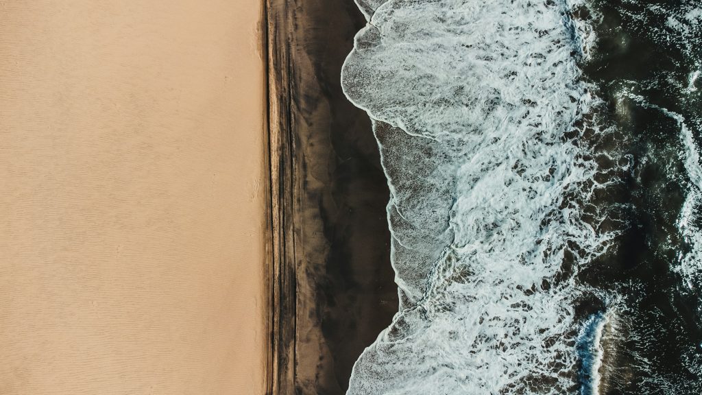 Vista aerea das ondas do mar quebrando sobre a faixa de areia clara