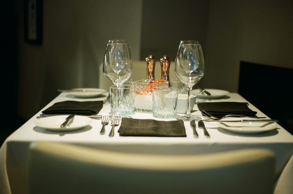 Mesa posta de restaurante com toalha de linho, talheres alinhados e taças de vinho vazias