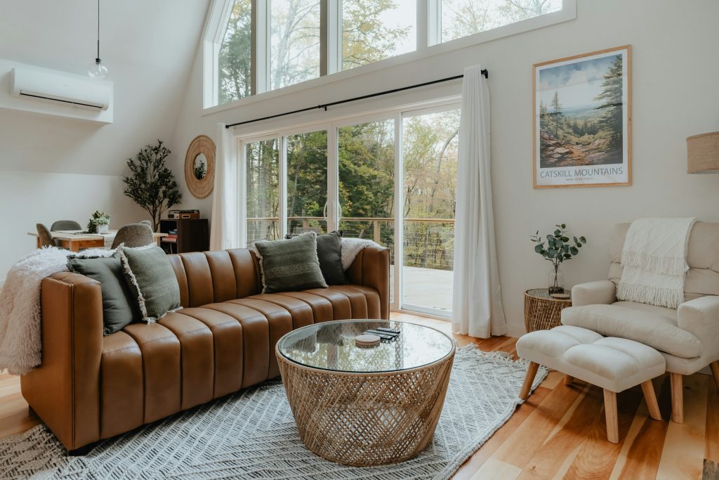 Sala de estar de chalé com poltronas de couro, piso de madeira e luz entrando pelos janelões