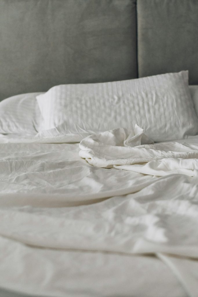 Cama de solteiro arrumada com lençóis e travesseiros de linho branco em quarto compacto de paredes claras