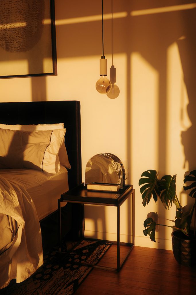 Luz quente de fim de tarde atravessando o quarto e iluminando a cama e uma planta ao lado