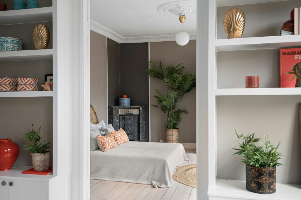 Cama arrumada em quarto com prateleiras de madeira tomadas por plantas verdes
