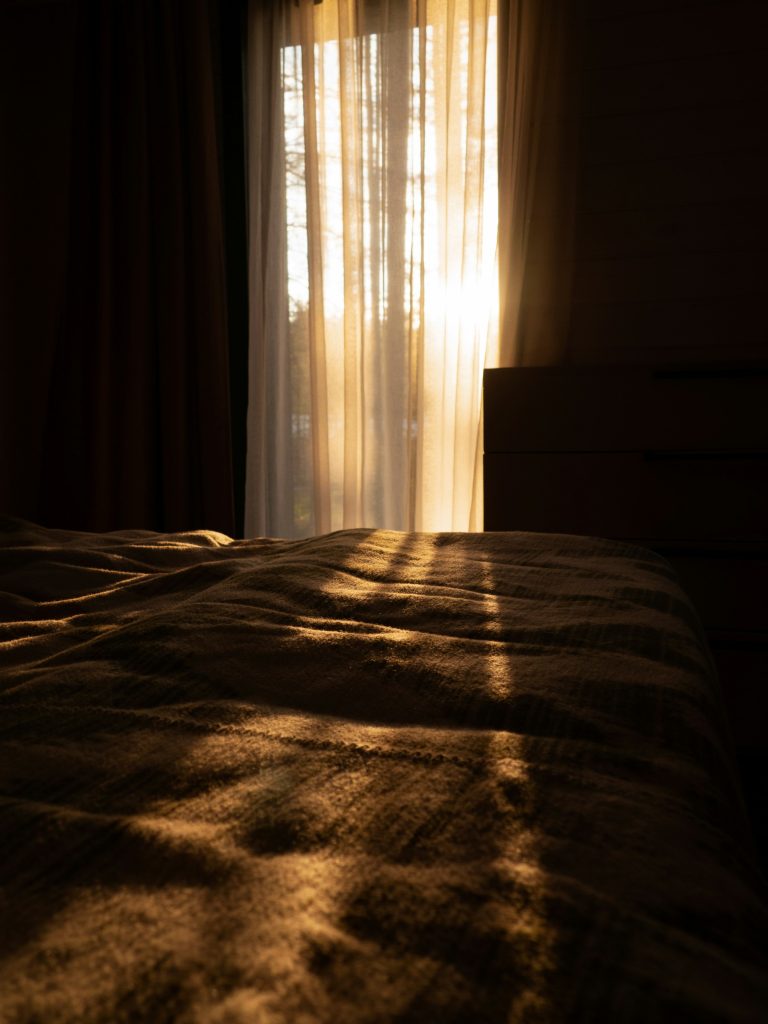 Sol de fim de tarde entrando pela cortina aberta sobre a cama, com a mata densa visível pela janela