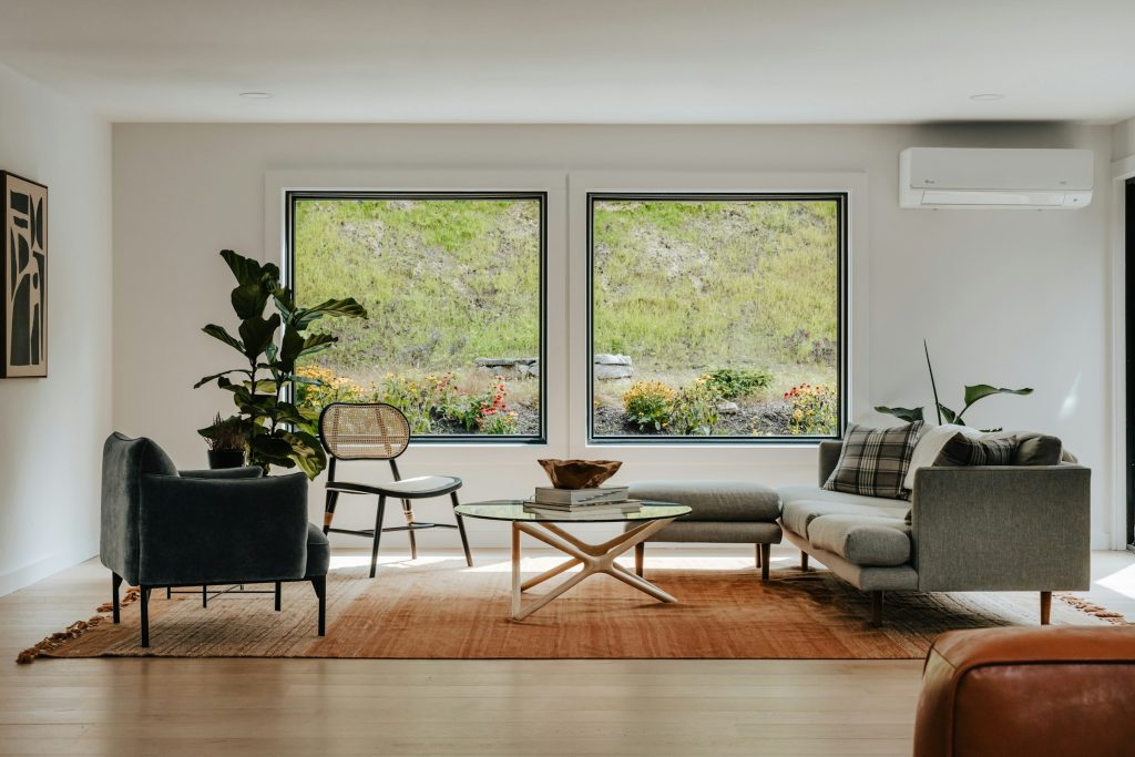 Sala ampla de villa com duas janelas altas, plantas e luz natural cobrindo o ambiente